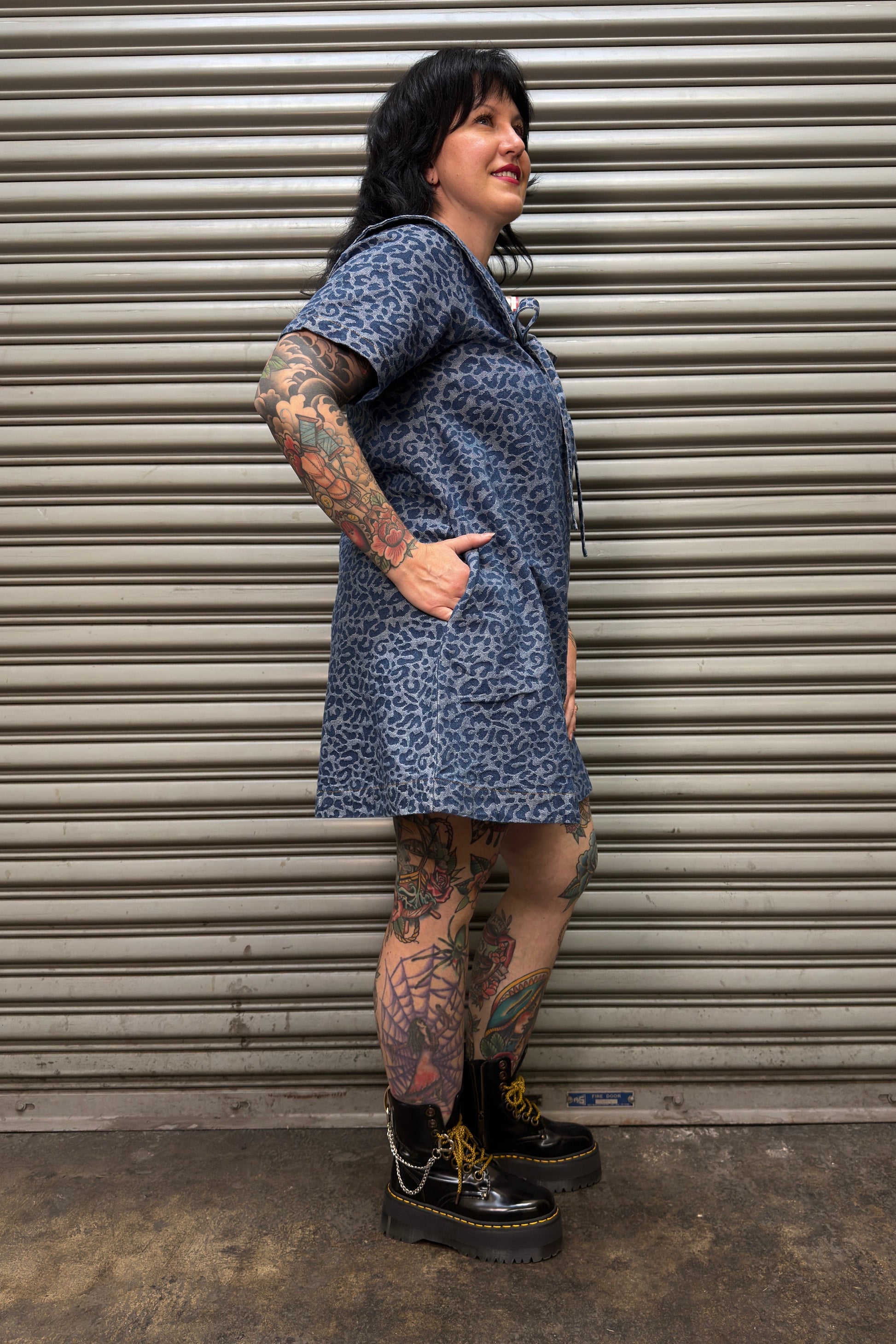 Person wearing a blue patterned dress standing in front of a metal shutter.